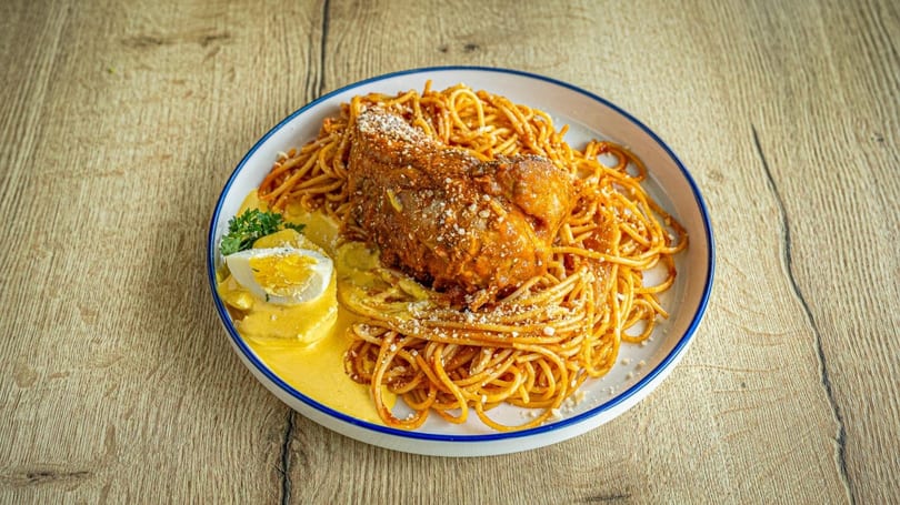 Spaghetti with a large piece of chicken, yellow sauce, and a hard-boiled egg on a white plate.