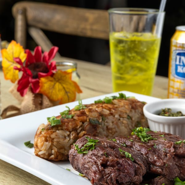 Grilled steak, rice with green onions, and a side of chimichurri sauce on a white plate.
