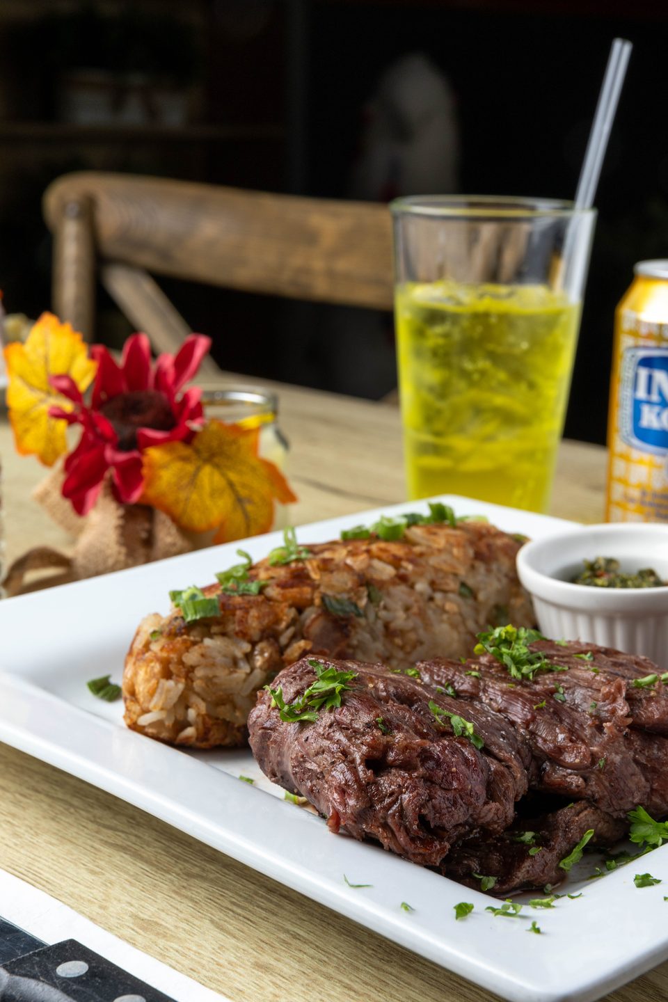 Grilled steak, rice with green onions, and a side of chimichurri sauce on a white plate.