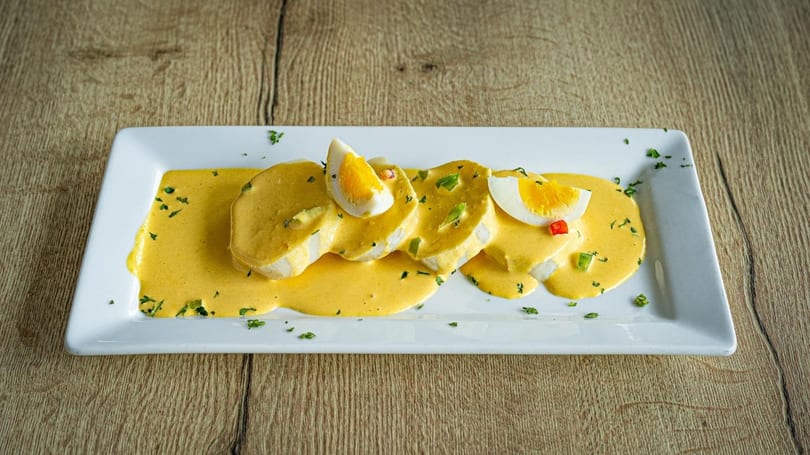 Sliced chicken breast covered in yellow sauce, garnished with hard-boiled egg and herbs on a white plate.
