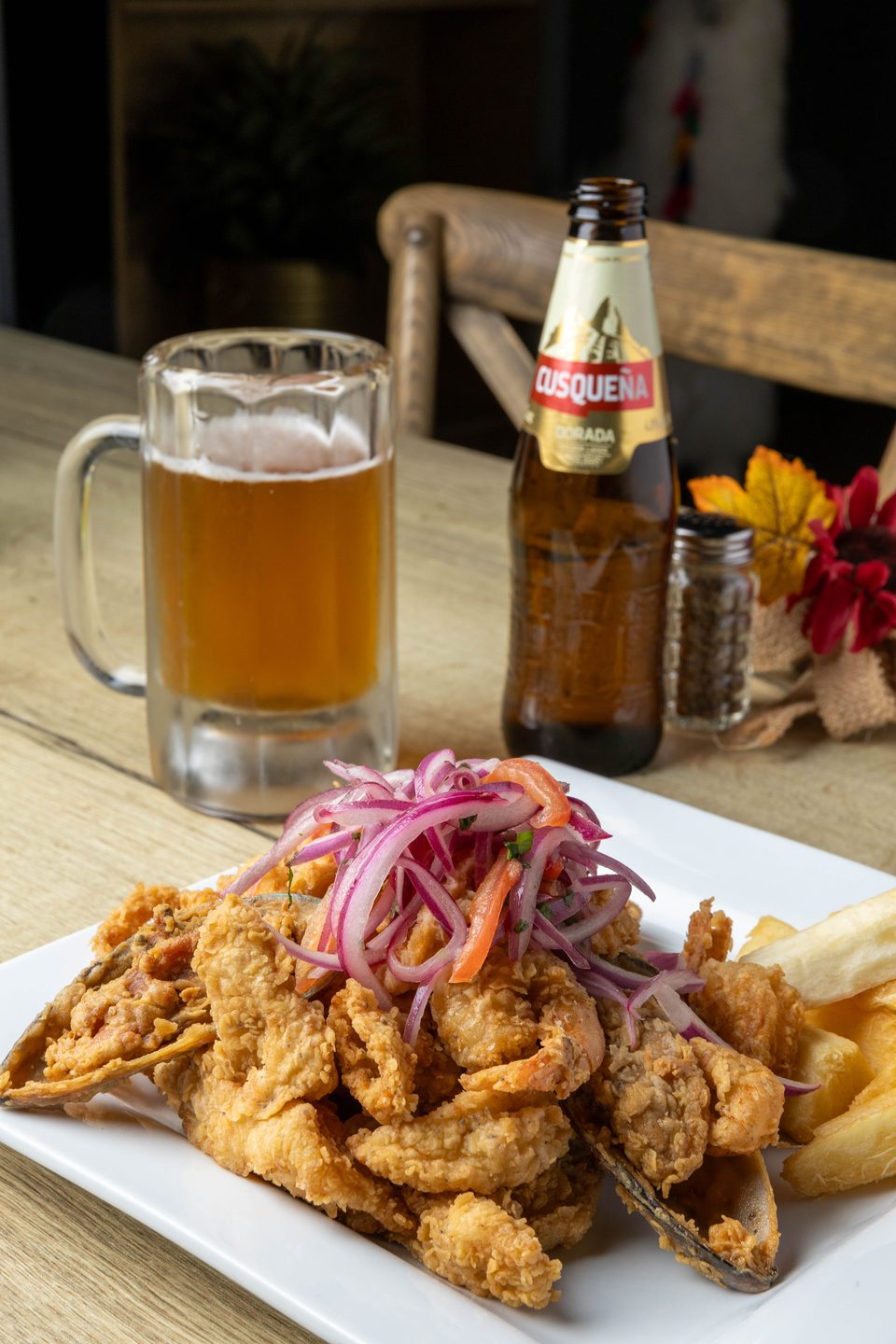 Fried seafood platter with red onion and pepper garnish, served with a beer mug and bottle.