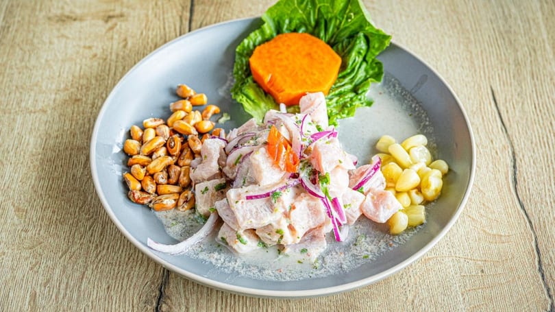 Peruvian ceviche with fish, red onions, corn, sweet potato, and lettuce on a grey plate.
