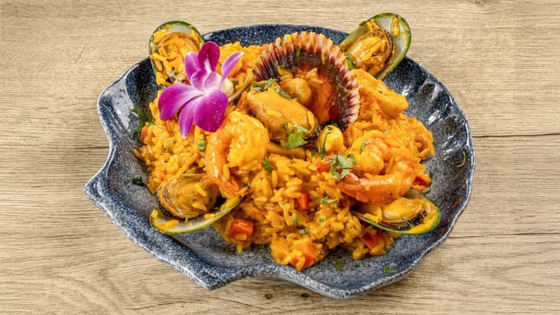 Seafood paella with shrimp, mussels, and a scallop, garnished with a purple orchid.