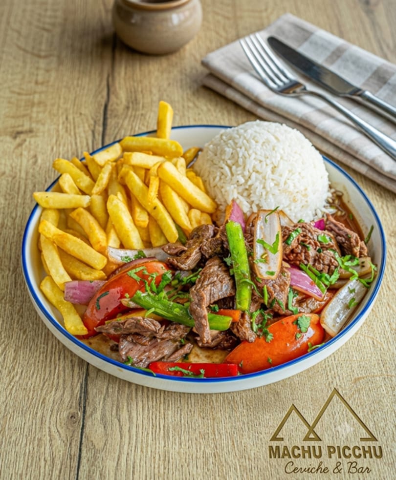 A plate of Lomo Saltado with steak, vegetables, french fries, and rice on a wooden table.