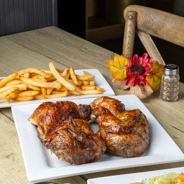 Plates of roasted chicken, french fries, and salad with dressing on a wooden table.
