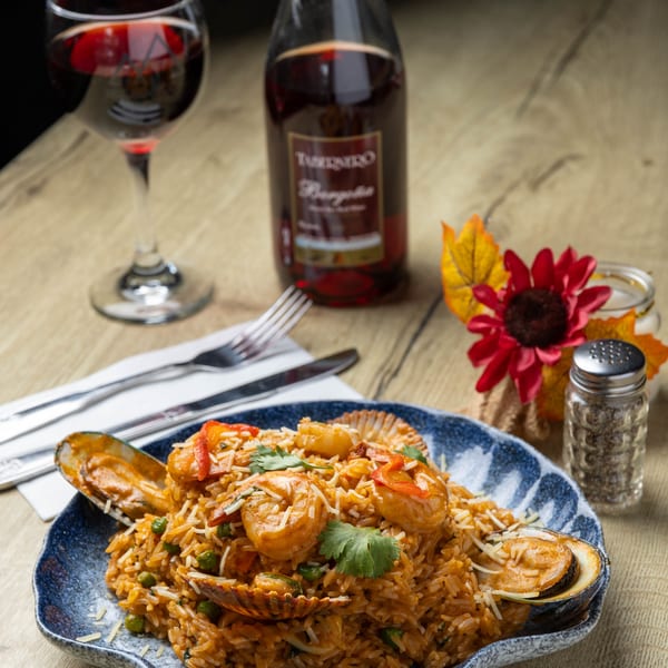 Seafood paella with shrimp, mussels, and scallops, served with red wine on a wooden table.