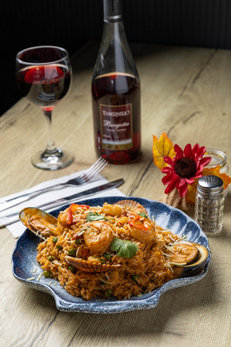 Seafood paella with shrimp, mussels, and scallops, served with red wine on a wooden table.
