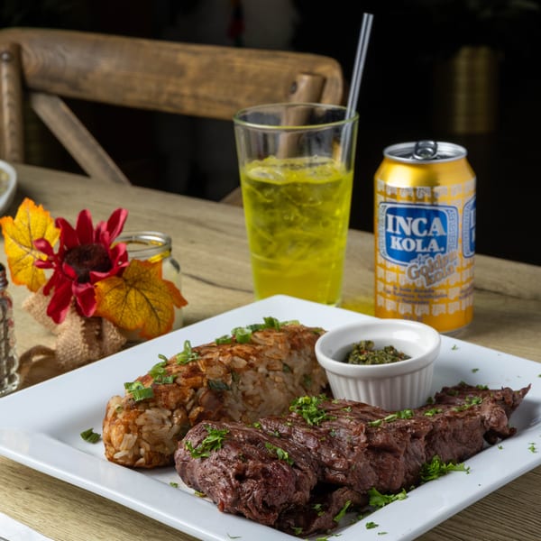 Grilled steak and rice with green onions, a side of green sauce, and Inca Kola.