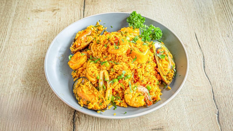 A vibrant seafood paella with mussels, shrimp, and squid, garnished with parsley, on a gray plate.